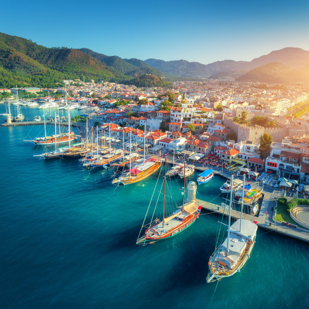 Aerial view of boats and beautiful architecture at sunset in Marmaris, Turkey. Colorful landscape with boats in marina bay, sea, city, mountains. Top view from drone of harbor with yacht and sailboat